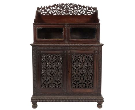 A 19th Century Anglo-Indian carved hardwood side cabinet,: in two parts, the upper part with a three quarter ledge back with 