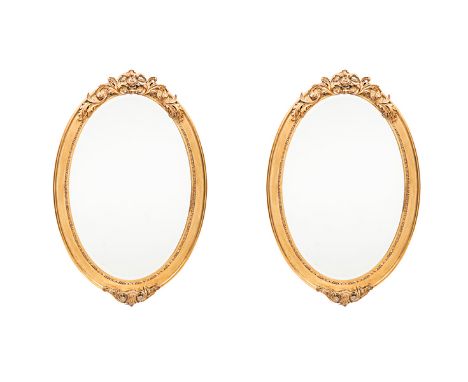 A PAIR OF GILTWOOD MIRRORS, 20TH CENTURY each oval beveled plate within a beaded surround, the frame surmounted by foliate-ca