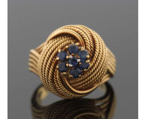 A sapphire set knot ring, the flowerhead cluster of small round sapphires set on top of a multi-strand textured knot that tap