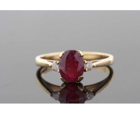 An 18ct ruby and diamond ring, the treated oval ruby in a four claw mount, set to either side with a small round brilliant cu