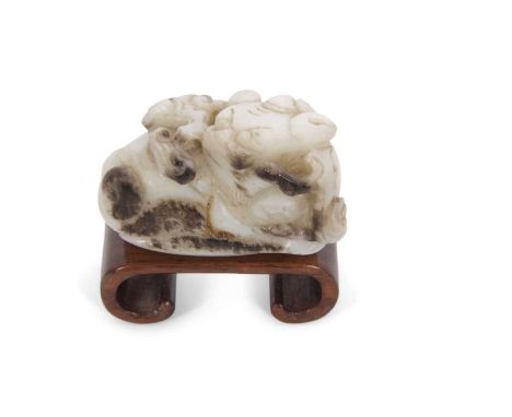 A jade carving of a dragon with brown occlusions on a curved wooden base, 5cm long