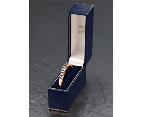 A 9ct gold hinged bangle having eleven graduated oval sapphires interspersed by twenty diamond chips in a scrolled setting to