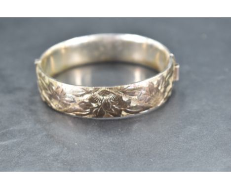 A silver hinged bangle having engraved floral decoration