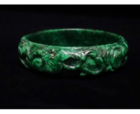 A mottled green jade bangle carved with two rabbits amongst leaf scrolls, diameter 7.5cm.