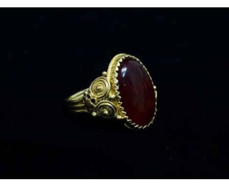 A continental Renaissance style high purity gold carnelian cabochon set ring, the shank with filigree and flowerhead applied 