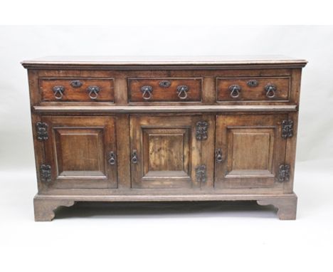 A GEORGIAN DESIGN OAK DRESSER BASE fitted with three drawers over three fielded panel cupboard doors with fancy iron handles,