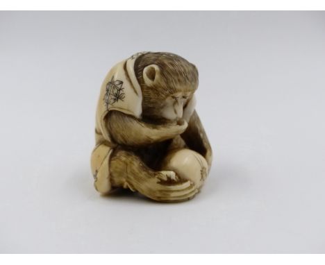 A SIGNED JAPANESE CARVED IVORY NETSUKE IN THE FORM OF A SEATED MONKEY OBSERVING AN INSECT ON A PIECE OF FRUIT. H.4cms.