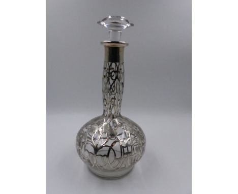 AN ART NOUVEAU GLASS DECANTER WITH OVERLAID WHITE METAL DECORATION. APPROXIMATE HEIGHT 28cms. 