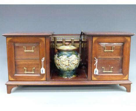 An Edwardian inlaid mahogany twin pedestal smoker's cabinet with brass rail, Doulton Lambeth lidded tobacco jar, pipes etc.  
