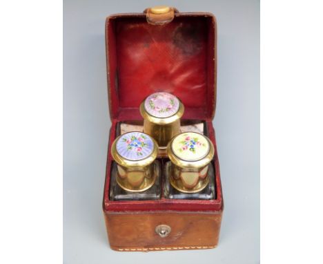 A late 19thC or early 20thC leather cased travelling set containing three glass bottles with floral guilloché enamel tops