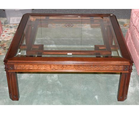 A reproduction mahogany glass topped coffee table with blind fret carving, raised on panel supports, 105cm by 105cm by 42cm 