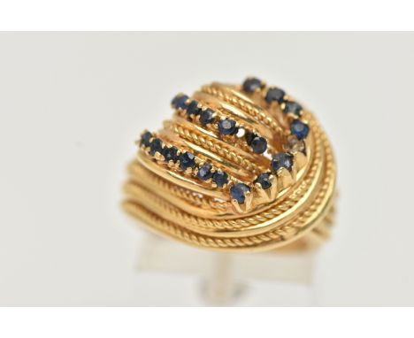 A YELLOW METAL GEM SET RING, a knot design dress ring, set with nineteen circular cut blue stones, comprised of paste, spinel