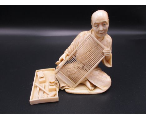 A Japanese Meiji period ivory okimono, modelled as an artisan screen maker at work, his tools by his side in a tray, signed t