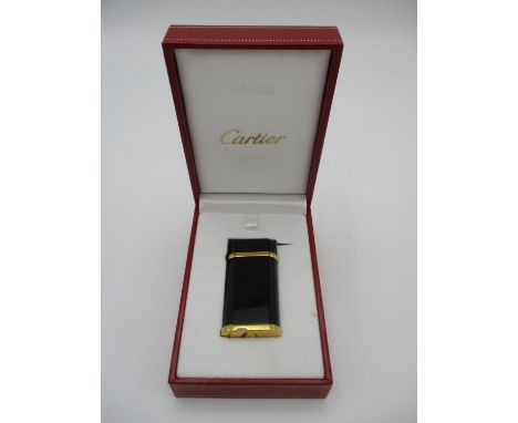A black lacquer and gold plated Cartier lighter, in presentation box, the black lacquer body with rounded edges and lid, the 
