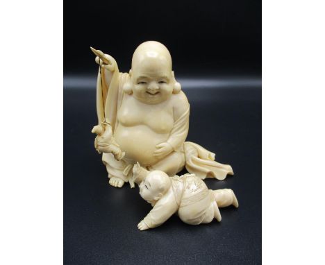 A Japanese Meiji period ivory okimono, modelled as Hotei the laughing Buddha, playing with an infant, signed in red to unders