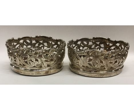 A rare pair of silver wine coasters attractively decorated with scrolls and leaves on oak panelled bases. London. By Hunt &am