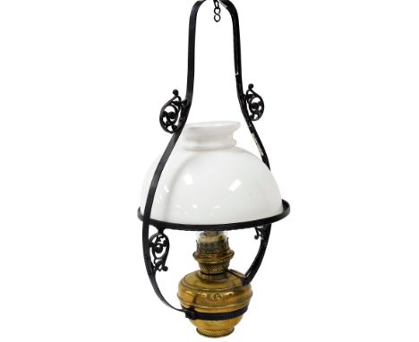 An early 20thC brass hanging oil lamp, in a scrolling cast iron frame, with glass chimney and white glass shade, 72cm high. 