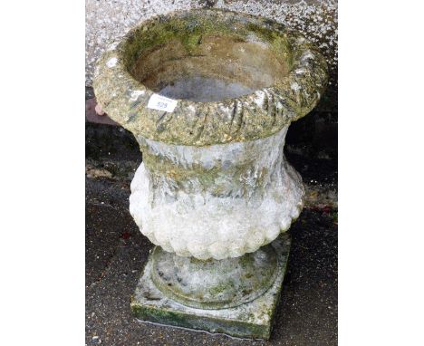 A reconstituted stone urn shaped planter, decorated with leaves and flowers, on a square base, 44cm high. 