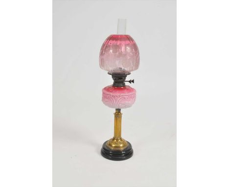 A Victorian oil lamp, with a fluted brass column supporting an opaque cranberry tinted glass fount, decorated with birds, flo