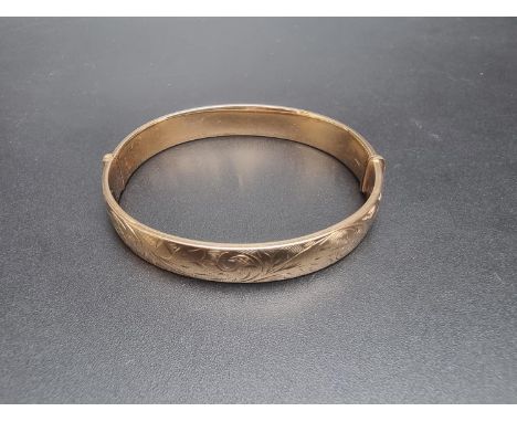 A 9ct gold hinged bangle, having chased floral decoration to one side, Birmingham 1973, 19.1g. 