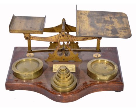 A SET OF LATE VICTORIAN OR EDWARDIAN LACQUERED BRASS POSTAL SCALES on a shaped wooden base, with turned brass weights from 4l