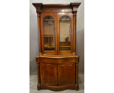 A Victorian Mahogany Bookcase, the moulded cornice above two arched glazed doors enclosing shelves flanked by turned pilaster