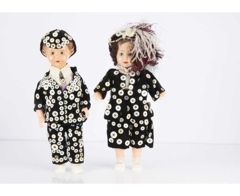 A pair of hard plastic dolls dressed as a Pearly King and Queen, with sleeping eyes and black velvet clothes decorated with m