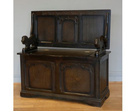 A mid 20th century monks bench, with hinged back, carved lion arm rests and hinged seat, opens to reveal a storage area, on b