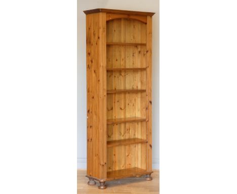 A pine Ducal opened fronted bookcase, five shelves over a lower shelf, arched top, on bun feet, 76 x 187 x 28cm, similar to t