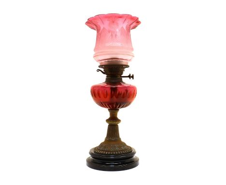 A Victorian cranberry glass oil lamp,with central chimney, leading to a graduated floral acid etched shade, above a slice cut