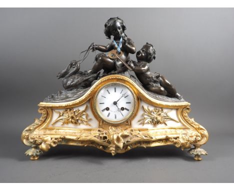A marble and ormolu mantle clock surmounted two putto and a swan, white enamel dial with Roman numerals and striking movement