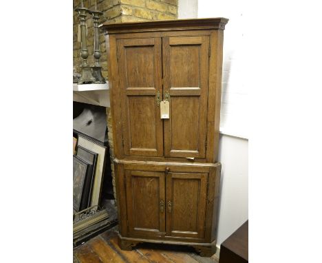 An early George III oak standing corner cupboard, having a cavetto moulded cornice above two pairs of fielded panelled cupboa