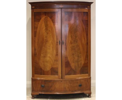 An Edwardian mahogany bowfront double wardrobe, the moulded Greek pattern cornice over a frieze inlaid with three conch shell
