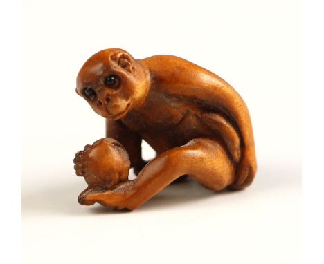 A Japanese carved wood netsuke, Meiji Period (1868-1912), modelled as a seated monkey, holding a fruit, signed to the undersi
