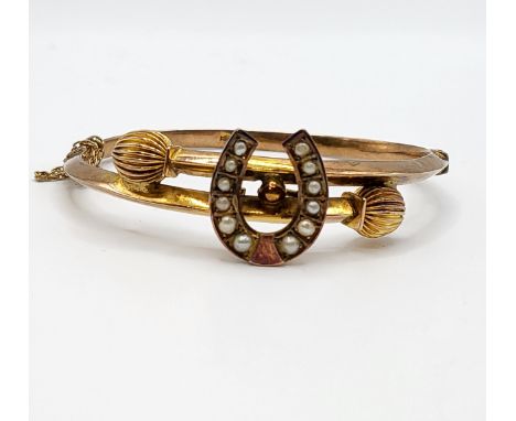 A late Victorian 9ct yellow gold bangle bracelet, the central horseshoe motif set with split seed pearls, with fluted termina