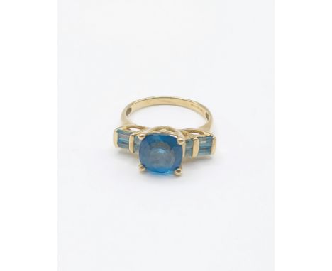 A 9ct yellow gold and blue topaz ring, set with a faceted cushion-cut bright blue topaz, four-claw set, the shoulders bar-set