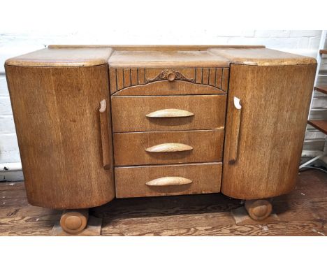 An Art Deco wooden sideboard with carved decoration, shelved interior, rounded doors and three drawers, supported on carved r