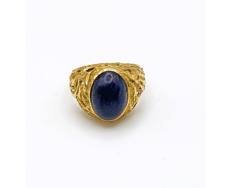 A yellow gold and lapis lazuli ring, set with an oval polished stone, within an ornate textured mount, indistinct mark to ext