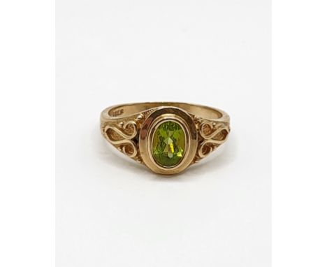 A 14ct yellow gold and peridot ring, set with a mixed oval-cut peridot, the shoulders with raised stylised decoration, size O