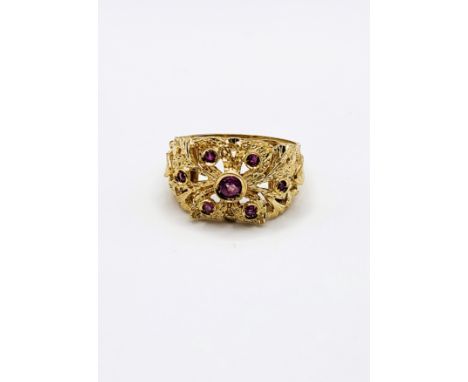 A yellow metal and ruby ring, centred with a collet-mounted ruby, and six smaller rubies, indistinct mark 750 to shank, size 