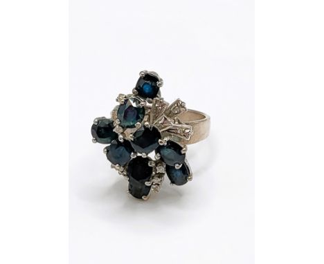 An 18k white gold, diamond, and sapphire asymmetric cluster ring, set with nine mixed round and oval-cut sapphires interspers