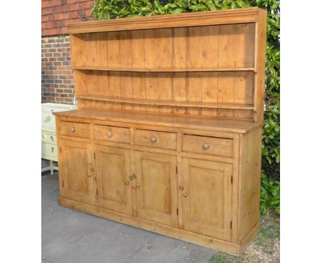 A 19th century pine large dresser, the boarded shelf back above four drawers and four cupboard doors raised upon a plinth, 21