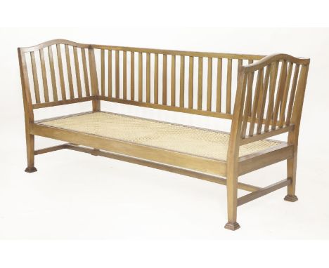 An Arts & Crafts mahogany settee,the arched ends with vertical splats, over a caned seat, with squab cushion,182cm wide