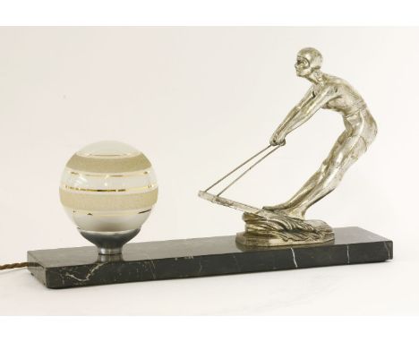 An Art Deco table lamp,mounted with a silvered spelter lady waterskiing, with a glass globe shade opposite, on a marble plint