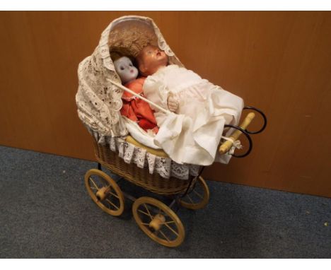A basketwork doll's pram containing three ceramic headed dressed dolls 