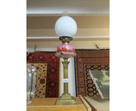 A brass Corinthian column oil lamp with pink glass floral decorated font and Sherwood's burner