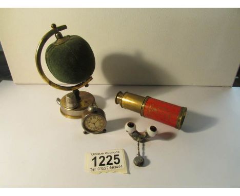 An Edwardian novelty globe pin cushioh/tape measure, a miniature alarm clock pencil sharpener, a small brass telescope and on