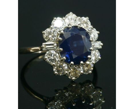 A white gold, sapphire and diamond oval cluster ring, with an oval mixed cut sapphire, claw set to the centre.  A border of b