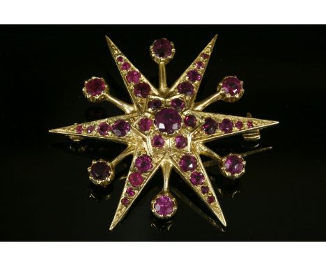 A 9ct gold ruby starburst brooch,an India star with a round cut, grain set, ruby cluster to the centre, graduating out to poi