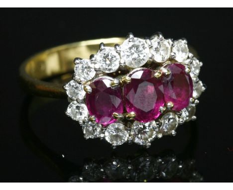 An 18ct gold ruby and diamond cluster ring, with three graduated oval mixed cut rubies, claw set in a row.  An outer border o